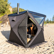 Silva portable wood-fired sauna on the beach with a person seated inside
